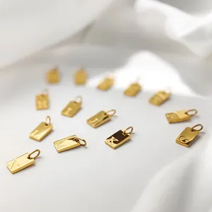 Close-up of golden stainless steel rectangular alphabet pendants on white fabric