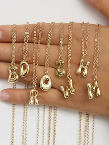 Detailansicht mehrerer 18K vergoldeter Halsketten mit klobigen Buchstaben auf der Hand