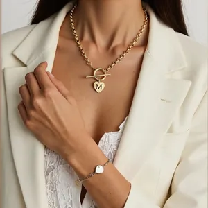 Détail d'un collier doré avec pendentif cœur lettre M et fermoir en T pour un look chic