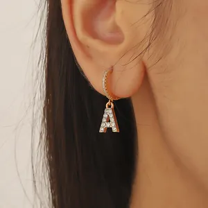 Boucles d'oreilles lettre A dorées avec zircons sertis portées par un mannequin