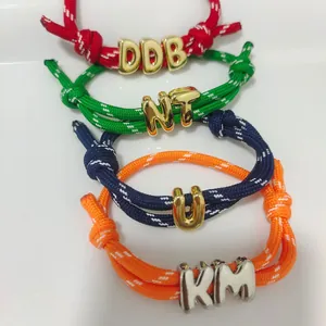 Close-up of colorful braided rope bracelets featuring adjustable sliders and metallic letter beads