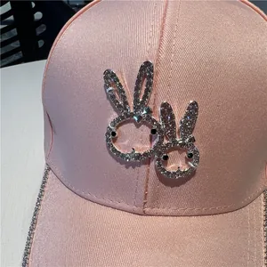 Close-up of pink satin baseball cap with sparkling rhinestone rabbits and brim detail