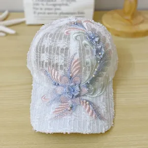 Detailed close-up of white lace baseball cap with floral embroidery and faux pearls