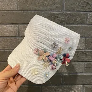 Detail of white knitted sun visor featuring colorful fabric flowers and rhinestone accents