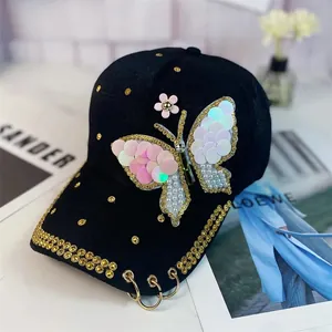 Detalle de gorra de béisbol negra con parche de mariposa de lentejuelas y aros dorados