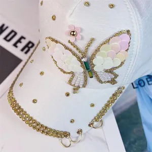 Detalle de gorra blanca con mariposa de lentejuelas, tachuelas doradas y aros metálicos
