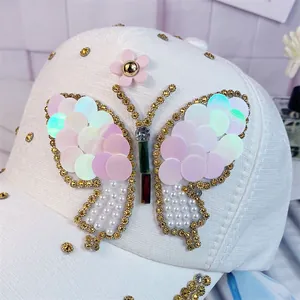 Detalle de gorra blanca con mariposa decorada con lentejuelas, perlas y brillantes de strass