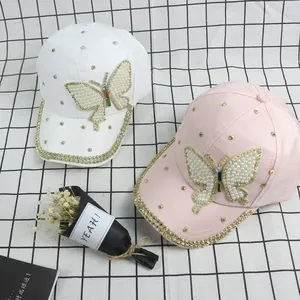 Detail of pink and white baseball caps featuring pearl butterfly and gold studs