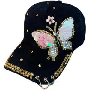 Gorra de béisbol negra con mariposa de diamantes, perlas y anillos metálicos en visera