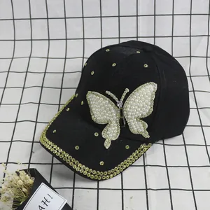 Detail view of a black baseball cap featuring a pearl butterfly and golden rhinestones