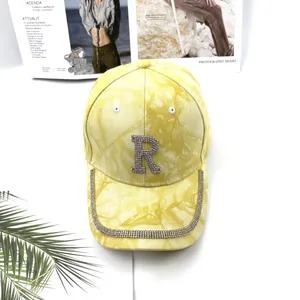 Détail d'une casquette tie-dye jaune avec lettre R en strass et bordure décorée