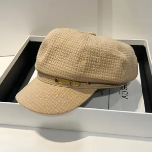 Detail van een beige bakkerspet met wafeltextuur en een gouden metalen gesp erop
