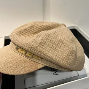 Detail van beige krantenjongenspet met gele lederen band en decoratieve metalen gesp op de zijkant