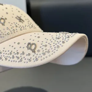Detailed close-up of beige baseball cap with sparkling rhinestones and CD logo design