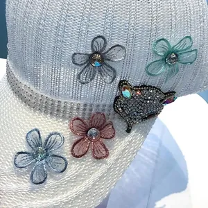 Dettaglio cappello bianco a maglia con fiori di strass e toppa gatto di paillettes