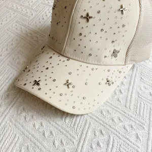 Close-up of beige mesh baseball cap with sparkling rhinestones and metal clover details
