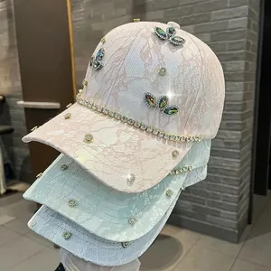 Dettaglio di cappellini in pizzo con farfalla di strass in rosa, menta e blu