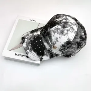 Close-up of black tie-dye baseball cap featuring rhinestones and golden logo on books