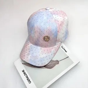 Gorra tie-dye con brillantes pedrería y logo M dorado sobre un fondo blanco minimalista