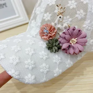Close-up of white lace baseball cap with 3D floral ornaments and deer brooch detail