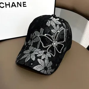 Detail einer schwarzen Spitzen-Cap mit weißen Blumen und einem großen Strass-Schmetterling