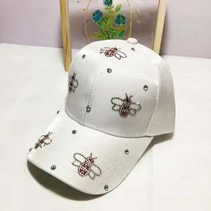 Detail of white satin baseball cap featuring rhinestone bee motifs and shimmering crystals