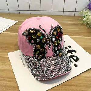 Détail de casquette rose en toile avec papillon en strass colorés et visière ornée