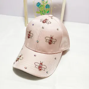 Detail of pink satin baseball cap featuring rhinestone bee patterns and sparkling crystals