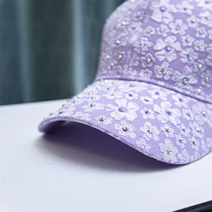 Detail of purple baseball cap with white floral lace embroidery and sparkling rhinestones