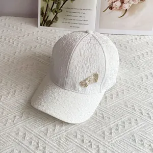 Close-up of white lace baseball cap featuring double heart metal and pearl accents
