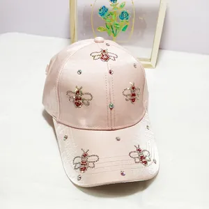 Detail of pink satin baseball cap featuring rhinestone bee embroidery and shiny finish