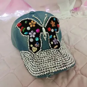 Détail d'une casquette en denim avec papillon en strass colorés et pendentif coeur