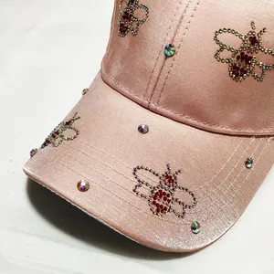 Macro view of pink baseball cap with sparkling rhinestone bee patterns and satin texture