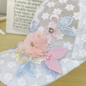 Dettaglio del cappellino in pizzo bianco con fiori 3D, perle e ricami di strass