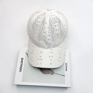 Détail d'une casquette en dentelle blanche avec strass colorés posée sur un magazine