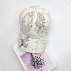 Detailansicht einer weißen Spitzen-Baseballkappe mit Schmetterlings-Strass und Blumenmuster