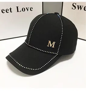 Détail d'une casquette en coton noir ornée de strass et d'une lettre M en métal doré