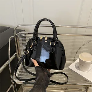 Elegant black glossy shell-shaped handbag with golden hardware and adjustable shoulder strap