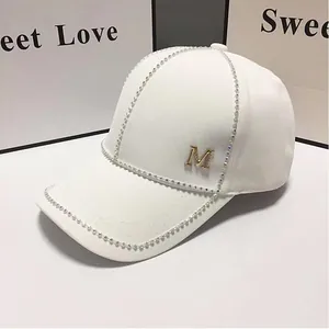 Détail de casquette blanche avec logo M doré et bordure en strass étincelants