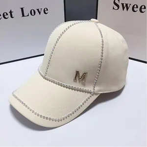Détail de la casquette de baseball crème avec strass et logo M doré sur le devant