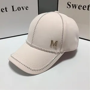 Détail de la casquette beige avec bordure en strass et logo lettre M dorée