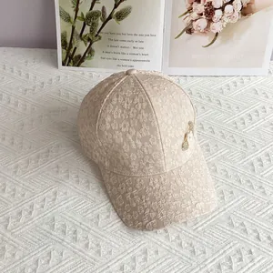 Close-up of floral lace texture and gold charm detail on a beige baseball cap