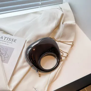 Glossy black dumpling bag with circular handle and gold chain on artistic background