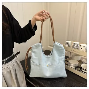 Detail of light blue canvas tote with brown braided rope handle and golden button pocket