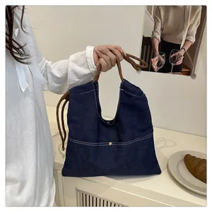 Detail of dark blue denim tote bag with brown knot handles and white topstitching