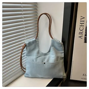 Detail of light blue denim tote bag with rope handles and metal buckle pocket