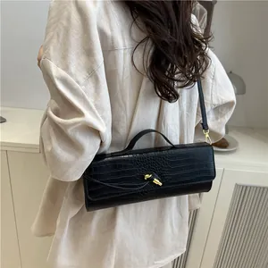 Fashionable black crocodile embossed baguette bag with gold twist lock shown on shoulder