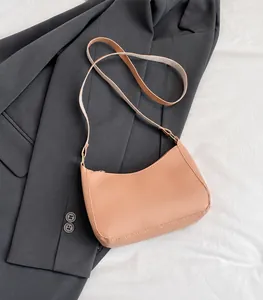 Close-up of pink crescent bag on a grey blazer showcasing smooth faux leather texture