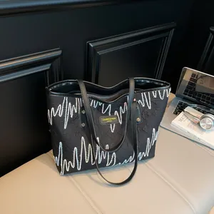 Large black tote bag with wave embroidery shown in a modern urban lifestyle setting