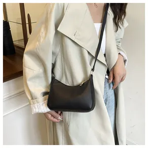 Chic black crescent underarm bag with gold zipper shown on a trench coat outfit